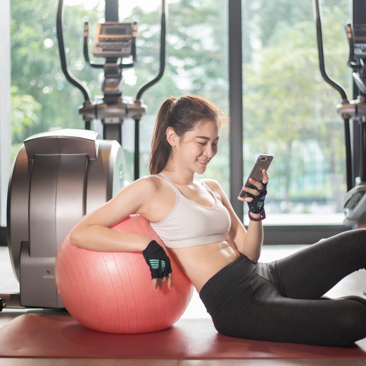Beautiful asian sport woman is playing smart phone in the gym relexing while workout